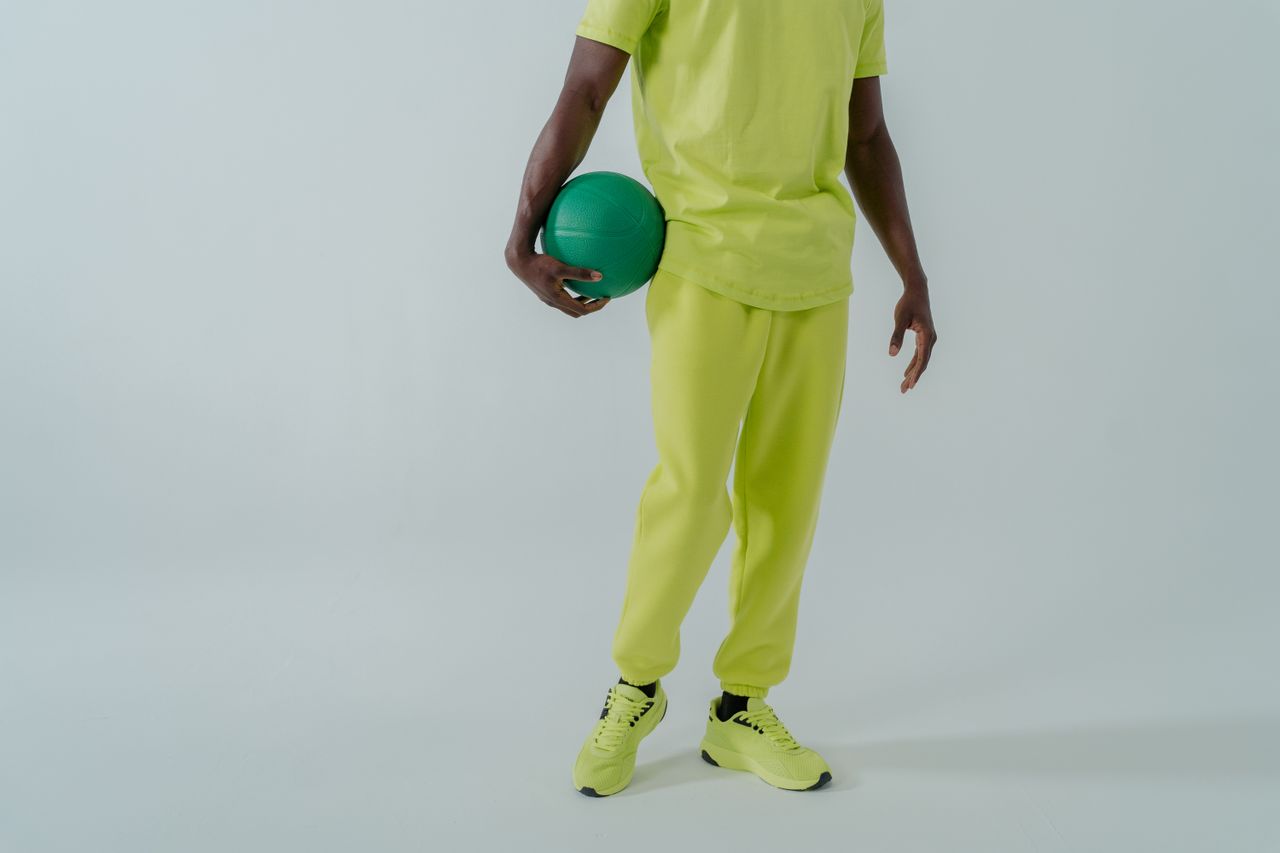 Stylish man in a lime green tracksuit holding a ball in a studio setting.